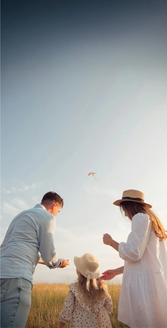 A family happily flying a kite in a lush field, with smiles on their faces and the sun shining brightly above them.